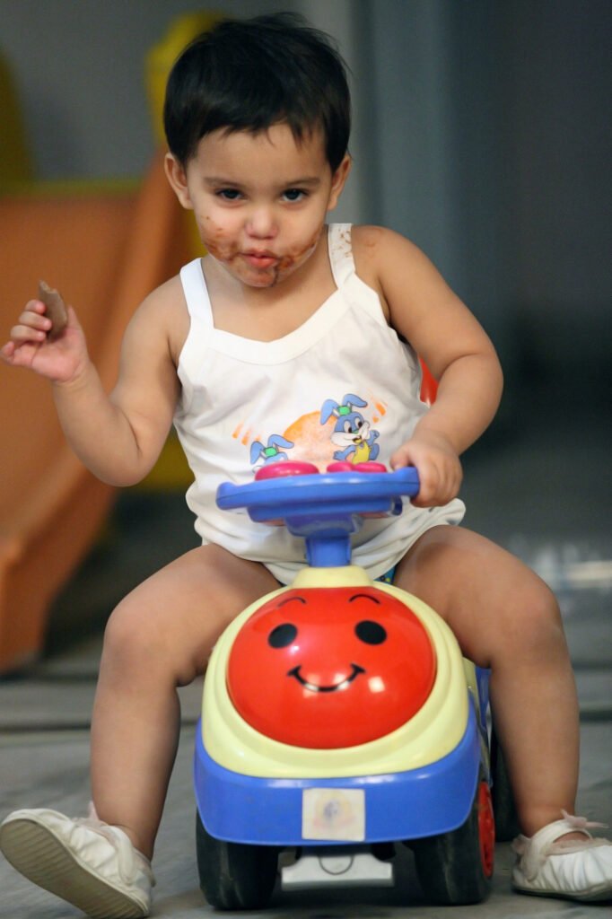 Lifestyle kids photography Auckland session of toddler riding toy car with chocolate on face