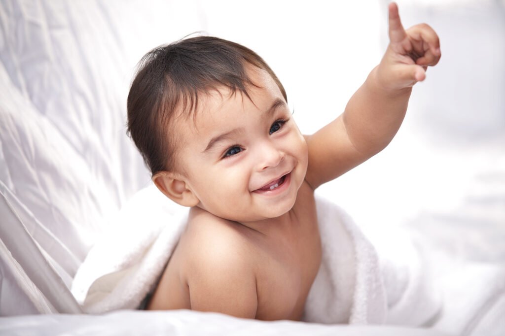 Childrens photographer Auckland session of smiling baby pointing up on white bed