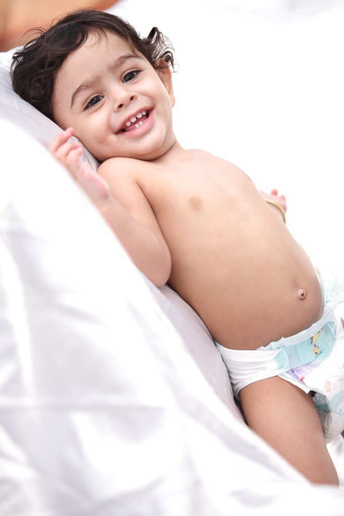 Toddler photographer Auckland session of happy baby lying down on white pillows