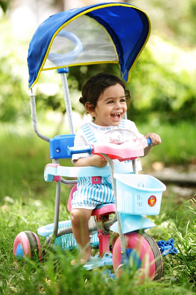 Outdoor baby photography Auckland session of smiling toddler riding blue toy tricycle