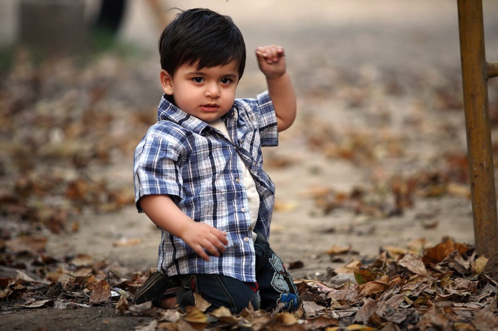 Childrens photographer Auckland session of little boy in plaid shirt sitting on dry leaves