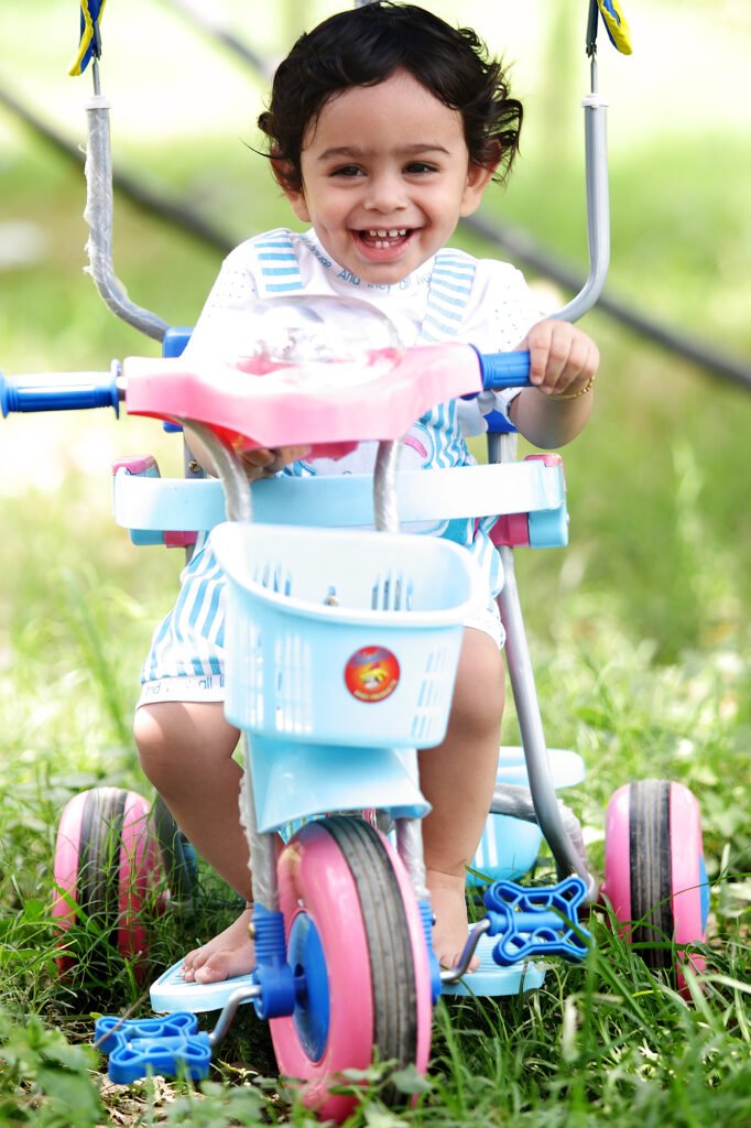 Infant photography Auckland session of happy baby boy riding toy tricycle