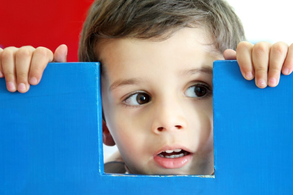 Educational marketing photography Auckland of little boy looking through blue playhouse window