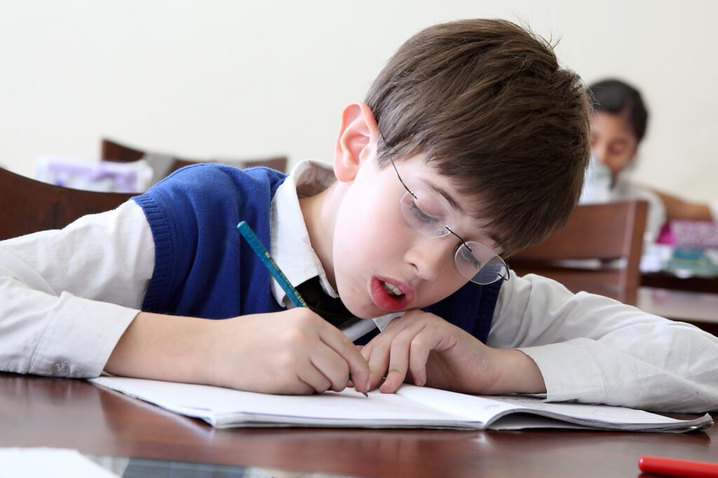 School prospectus photography Auckland of schoolboy with glasses writing at desk