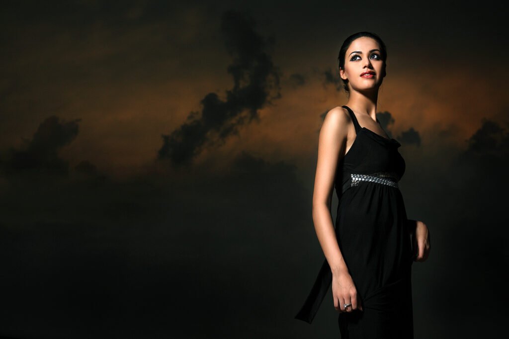 Cinematic outdoor portrait of a female model wearing a black dress against a dramatic sunset sky during a professional photoshoot by Auckland photographer Jassa Studio