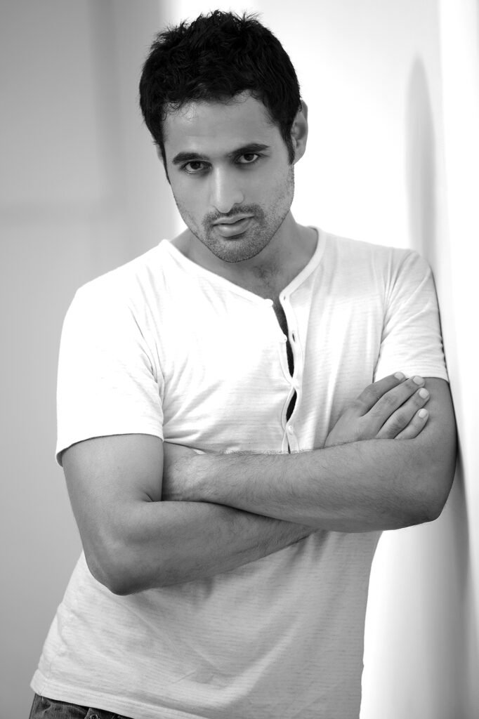 Black and white portrait of Australian actor Nicholas Brown with crossed arms leaning against a studio wall during a photoshoot by Auckland photographer Jassa Studio.